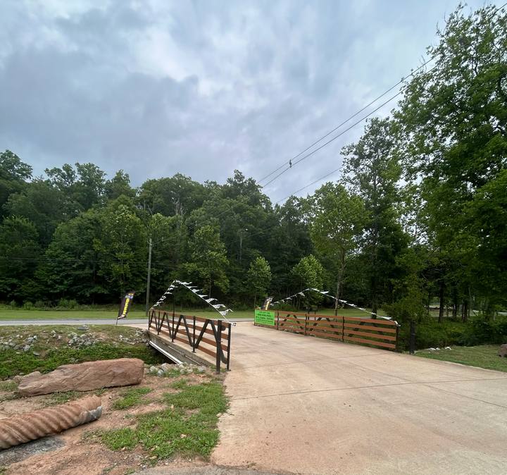 A paved drive crossing a bridge with wooden rails, checkered flags strung overhead