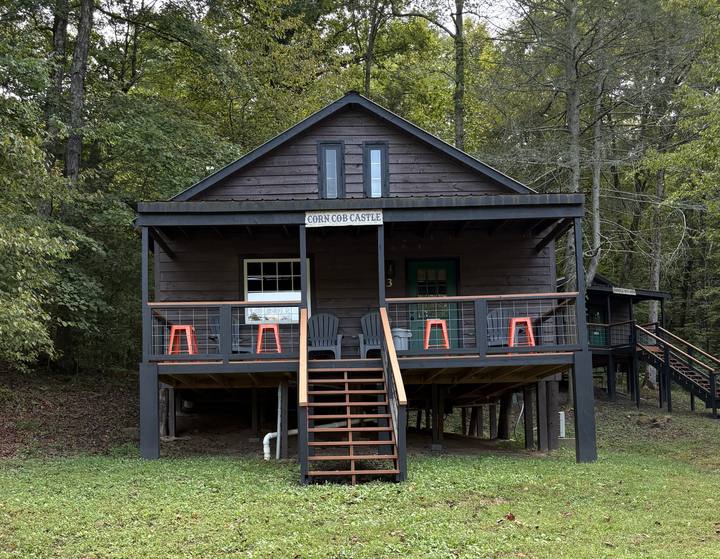 The Corn Cob Castle, a cabin with a covered porch, orange stools along the rail and stairs up the middle