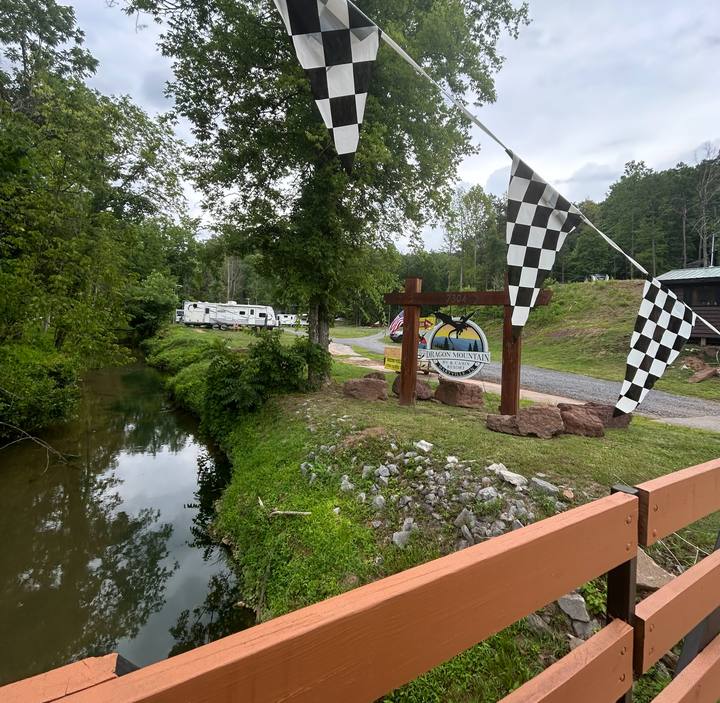 Checkered flags strung over the creek from a wooden bridge, RVs parked beyond
