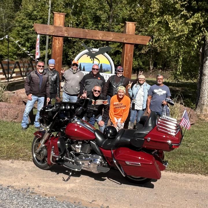 A group of riders gathered around a red touring motorcycle in front of the Dragon Mountain entrance sign