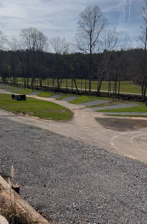Gravel RV pads with grass strips along a curving paved drive, bare trees beyond