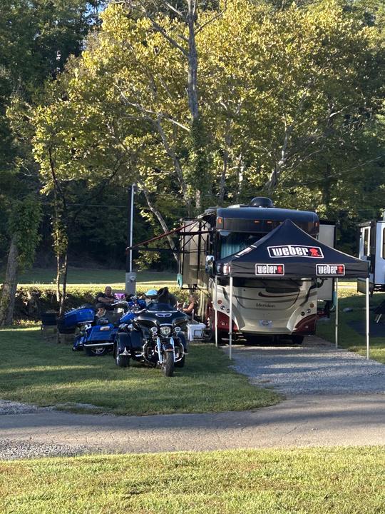 A motorhome with a canopy tent out front and touring motorcycles parked on the grass beside it