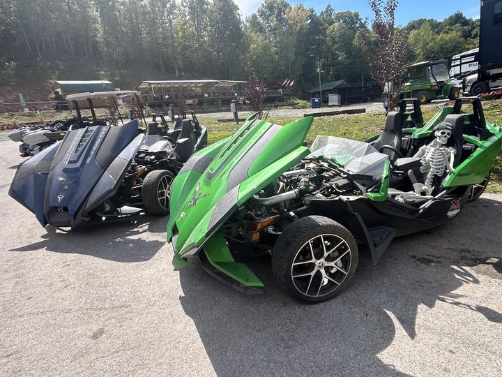 Two three-wheel roadsters parked in the lot, a toy skeleton sitting in the green one